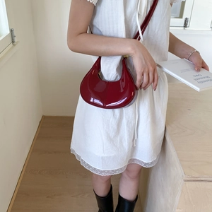 Détail du sac demi-lune rouge foncé en cuir verni brillant avec finitions dorées