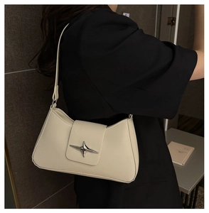 Detail of a minimalist cream baguette bag featuring a silver star metallic ornament