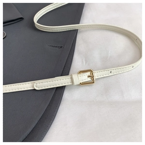 Close-up of cream faux leather belt with a gold pin buckle on dark grey blazer