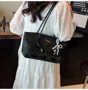 Close-up of black snake-embossed leather tote with a large white pearl bow pendant