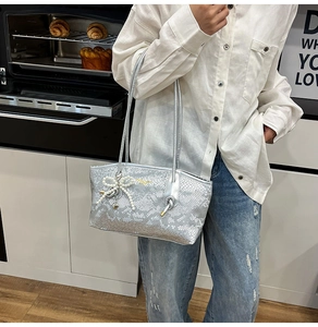 Silver snakeskin tote bag with pearl bow pendant in a modern lifestyle home setting