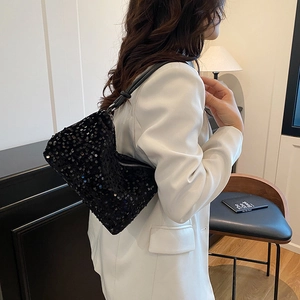 Fashionable black sequined shoulder bag with glossy finish on a white blazer model