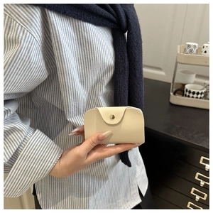 Detail shot of a small cream coin purse with a round gold buckle held by a hand
