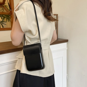 Minimalist black glossy leather vertical phone bag shown on model in a chic indoor setting