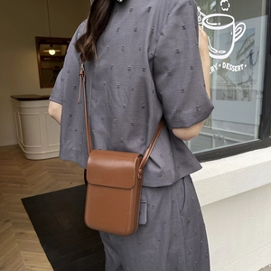 Minimalist brown leather crossbody phone bag shown on a model in a casual outdoor setting
