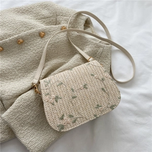 Détail de broderie florale sur sac besace tressé beige posé sur une veste