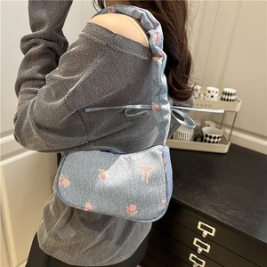 Light blue denim armpit bag with pink rose and bow prints shown on model shoulder