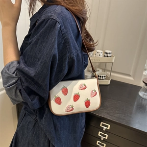 White shoulder bag with strawberry print and brown leather trim worn by a model