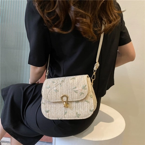 Détail du sac selle tissé avec broderie florale verte et fermoir métallique en U doré
