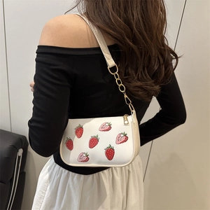 White underarm bag with red strawberry print and gold chain strap shown on model