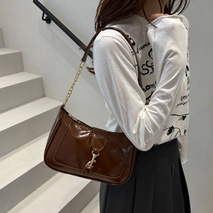 Close-up of brown glossy shoulder bag featuring a vintage golden piston buckle and chain