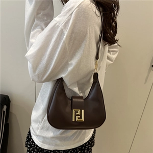 Brown leather crescent underarm bag with gold metal hardware shown on a model's shoulder