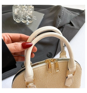 Detail of woven shell handbag with white leather handles and gold double zippers