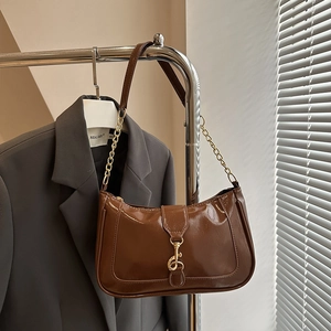 Detailed view of brown patent leather crescent bag with gold chain and metal buckle