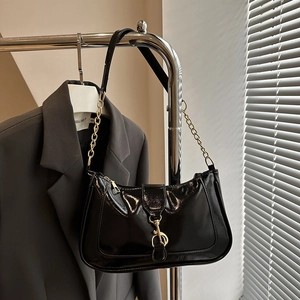 Detail of black patent leather shoulder bag with gold metal buckle and chain strap