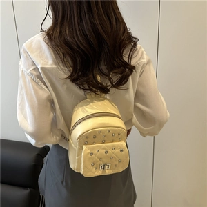 Chic beige quilted mini backpack with rivet accents shown from a rear wearing perspective