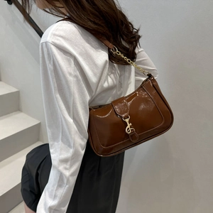 Brown patent leather shoulder bag with gold chain strap shown on model in minimal setting