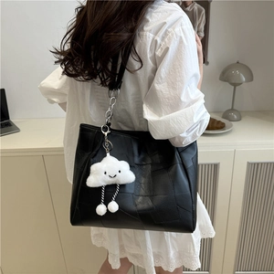 Fashionable black patchwork tote bag with a smiling cloud plush charm shown on shoulder