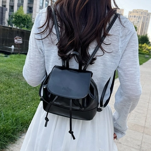 Glossy black mini leather backpack with mim logo shown on white outfit outdoors