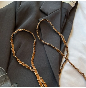 Close-up of golden metal chain interwoven with brown leather strap on a grey suit jacket