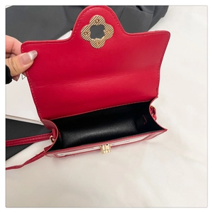 Detail view of red leather crossbody bag featuring gold floral metal clasp and black lining