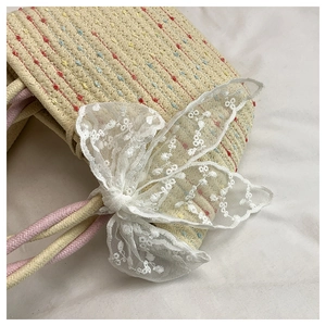 Detailed close-up of woven straw handbag featuring colorful thread and a large lace bow