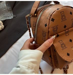 Close-up of brown mini bear print backpack with golden chain and pebbled leather texture