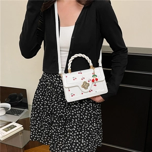 White cherry print crossbody handbag with floral lock and woven handle on a model