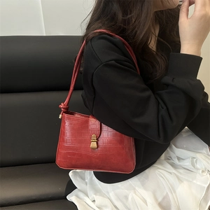 Sac sous le bras rouge foncé à motif crocodile et boucle dorée porté par un mannequin
