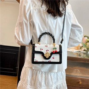 White crossbody bag with red cherry prints, rope handle and gold floral clasp