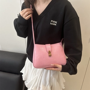 Sac bandoulière carré rose à motif croco avec boucle en bronze porté par un mannequin
