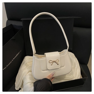 Détail du sac baguette en cuir blanc avec boucle nœud dorée posé sur une boîte noire