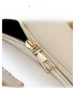Detailed view of the smooth golden metal zipper on a minimalist cream-colored tote bag