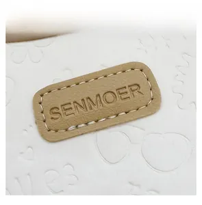 Detailed close-up of embossed heart patterns and leather logo patch on a white tote bag