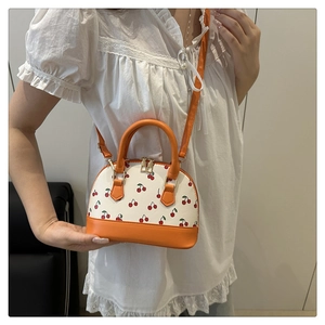 Detail of cherry print shell bag with orange leather handles and gold zippers