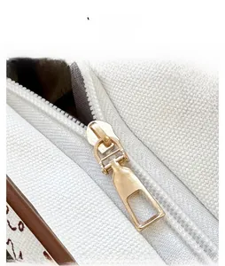 Detail display of smooth golden metal zipper and brown leather trim on canvas tote bag