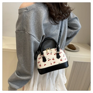 Detail of a cherry print shell bag featuring black leather handles and crossbody strap