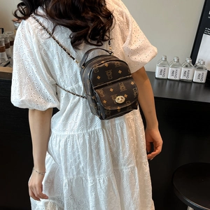 Brown mini backpack with bear prints and chain strap shown on a model in white dress