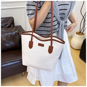 Detail of white embossed tote bag featuring brown leather straps and cartoon patterns