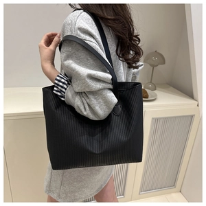 Detail of a large black tote bag with vertical pleated texture shown on model's shoulder