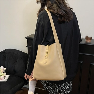 Minimalist beige leather bucket bag for women with wide shoulder strap and metal clasp