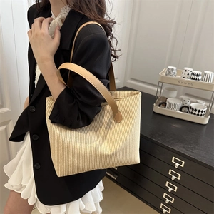 Chic beige woven tote bag with brown leather straps shown on a shoulder in daily style