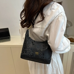 Chic black snakeskin embossed shoulder bag with gold logo lettering on a female model