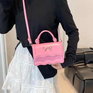 Pink leather handbag with wave edges and silver bow clasp shown on a model