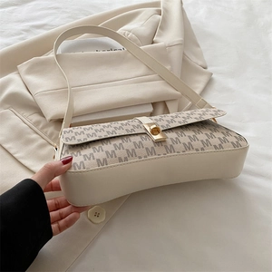 Détail du sac crème avec rabat monogramme et fermoir doré posé sur un tissu blanc