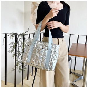 Detail der silbernen Stepptasche mit glänzender Metallstruktur und breiten Bandgriffen