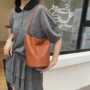 Orange textured leather bucket bag with silver chain worn by model in street setting