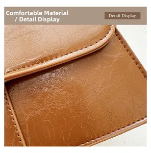 Detail display of brown faux oil wax leather texture and stitching on crossbody bag