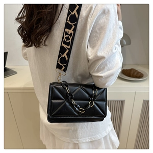 Detail of black quilted crossbody bag with patterned wide strap and decorative chain