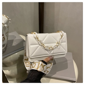 Close-up of white quilted crossbody bag with stylish gold chain and wide patterned strap